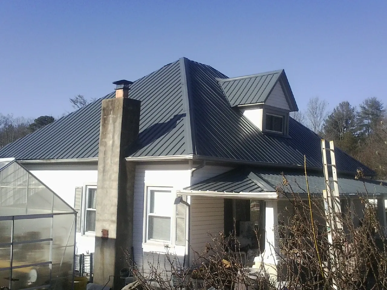 Dark blue standing seam metal roof on a white farmhouse with dormer — Slate & Tile Roof Repair by Roofing Brothers in Slinger