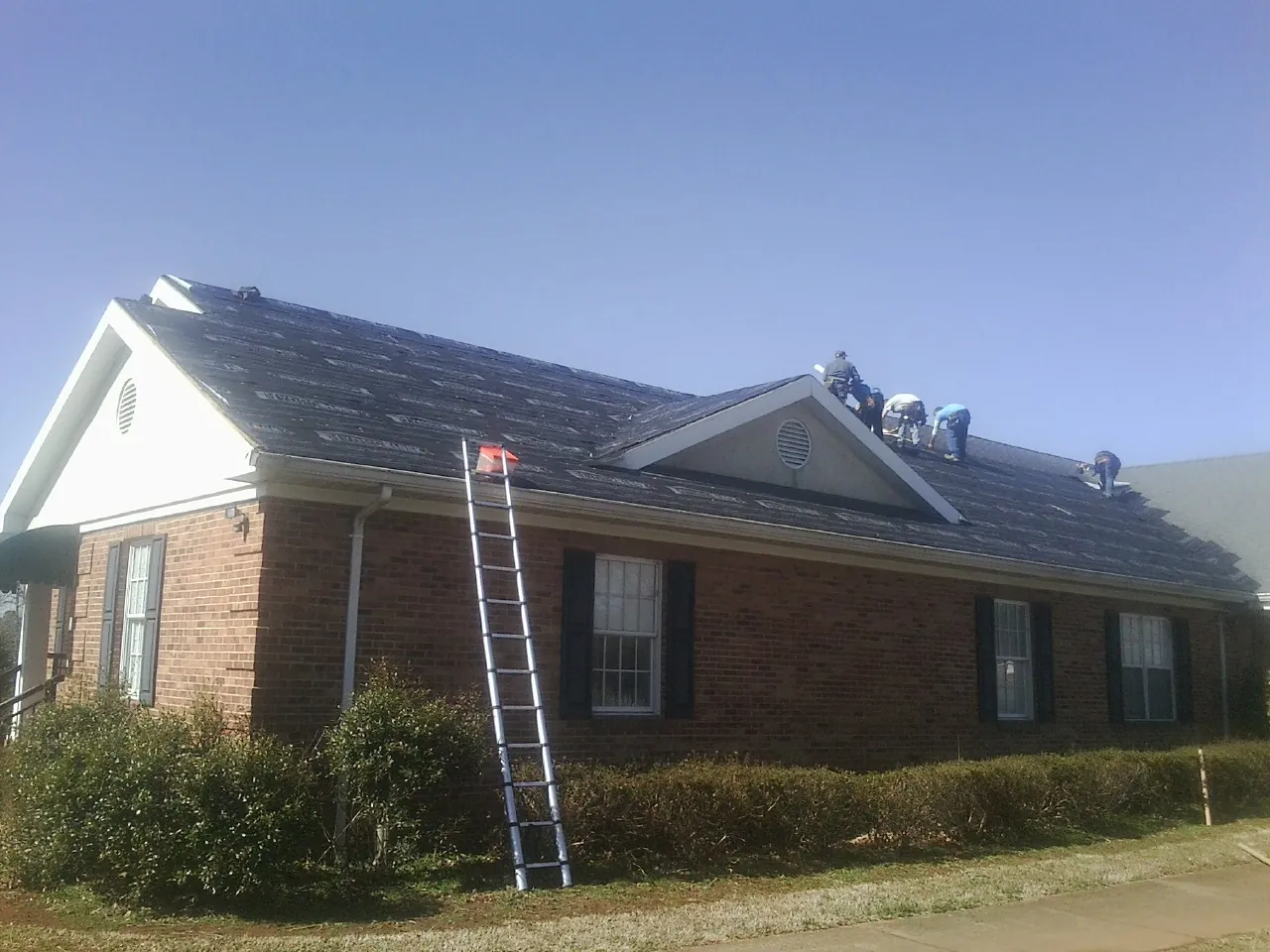 Crew tearing shingles off a brick ranch roof with a ladder set — Emergency Roof Repair work by our crew in Slinger