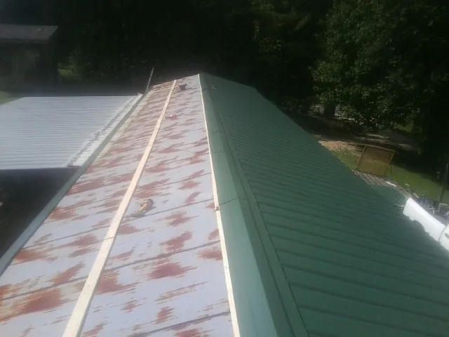 Old rusted panels beside newly installed green metal roofing — Wind Damage Roof Repair by Roofing Brothers in Slinger