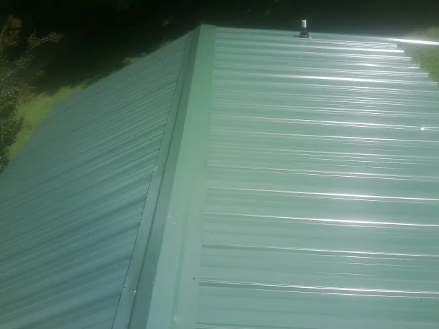 New green metal panels meeting at the ridge of a roof — Flat Roof Repair work by our crew in Slinger
