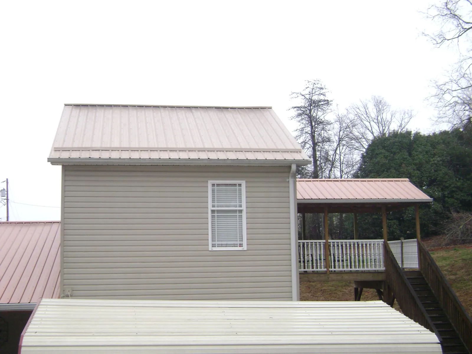 Tan metal roofs on a two story addition and attached porch, from a Roof Replacement job in Slinger