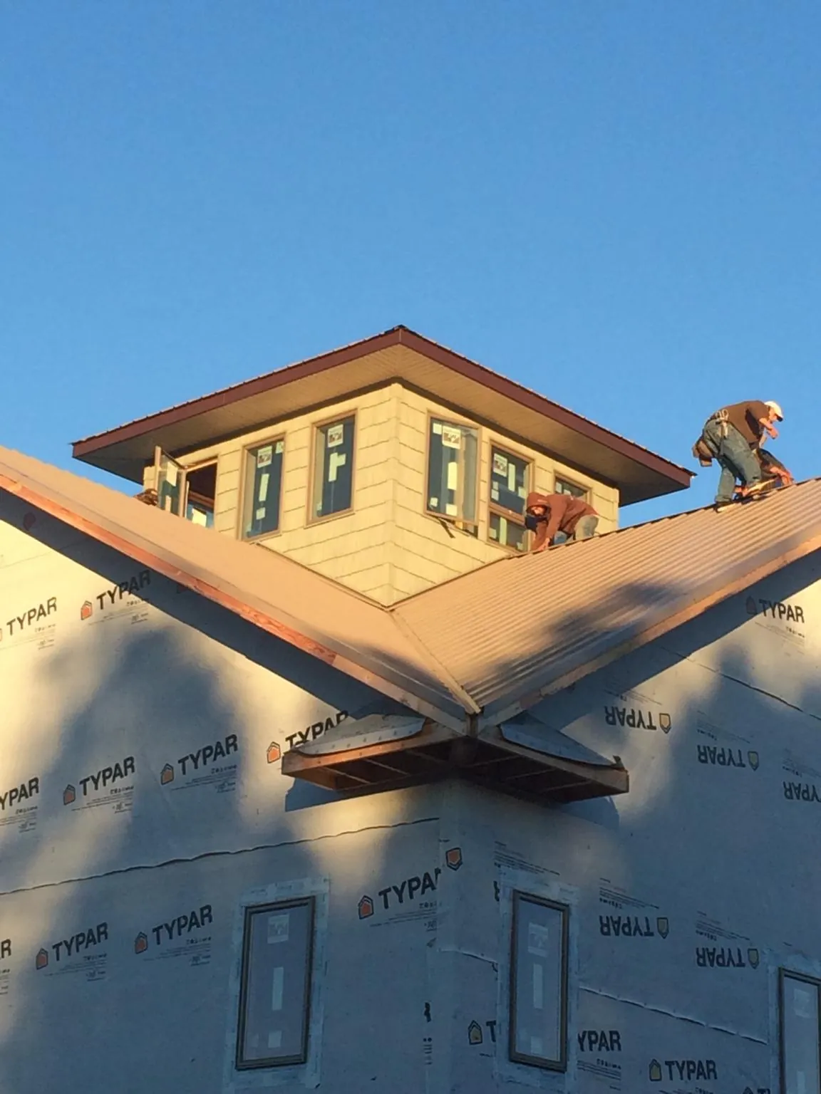 Roofers working around a rooftop cupola on a new metal roof at sunset — Roof Waterproofing in Slinger by Roofing Brothers